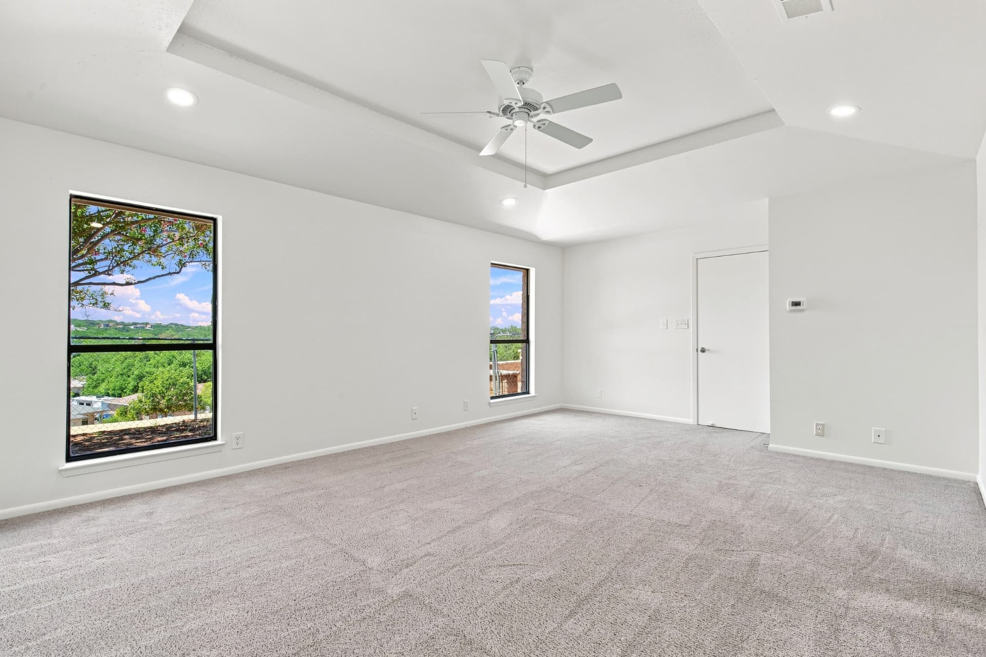 Primary bedroom with tray ceiling and picture window to the treetops