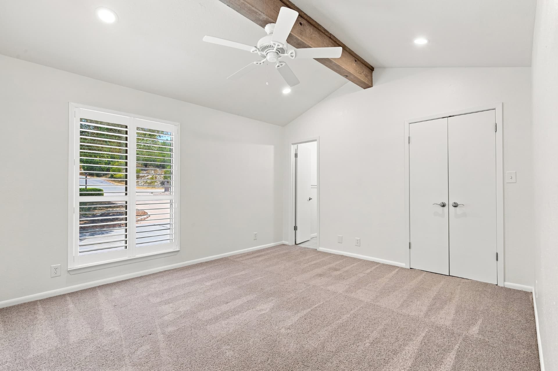 Bedroom with vaulted ceiling, wood beam, and plantation shutters