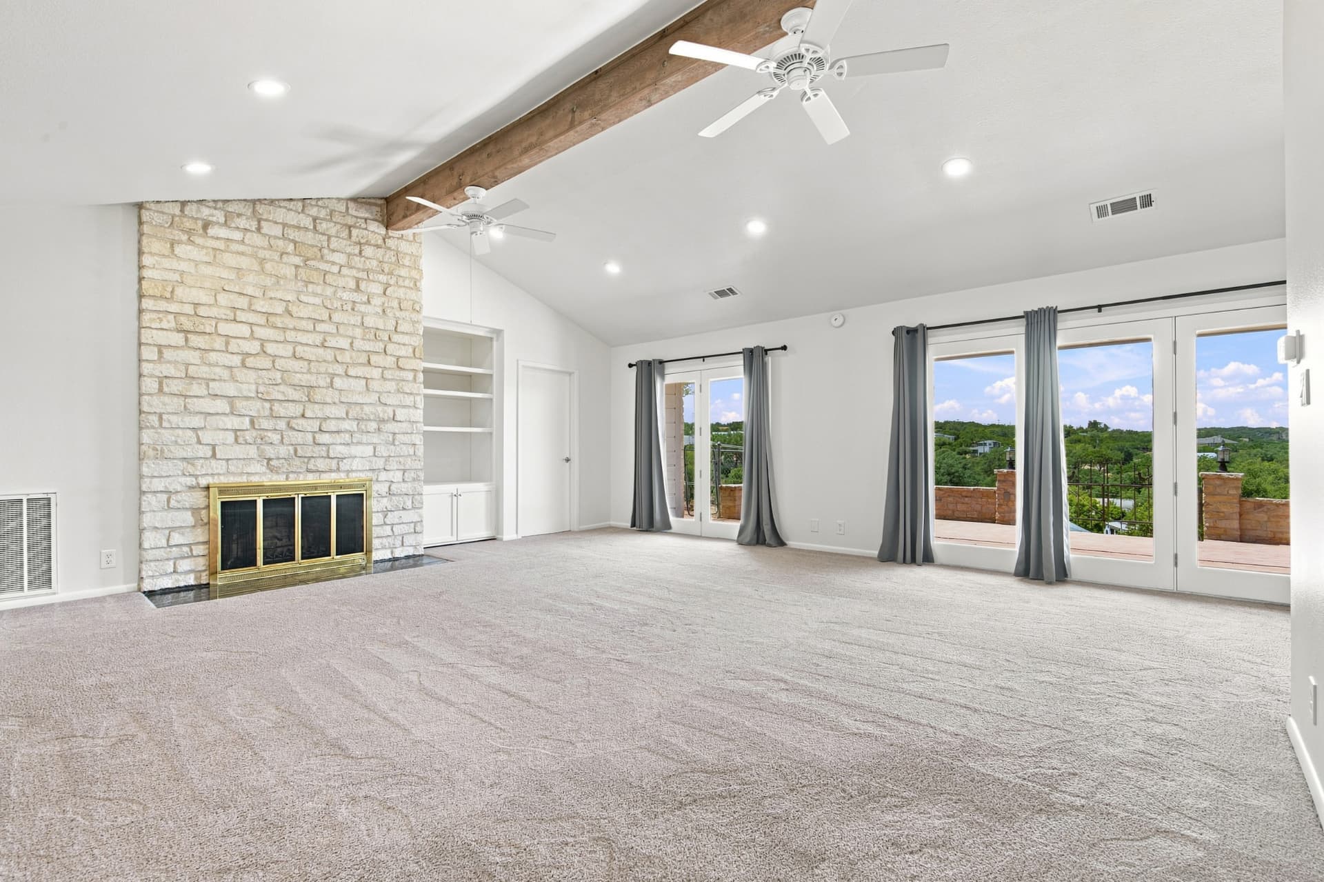 Living room with stone fireplace, beamed ceiling, and glass doors to the hills